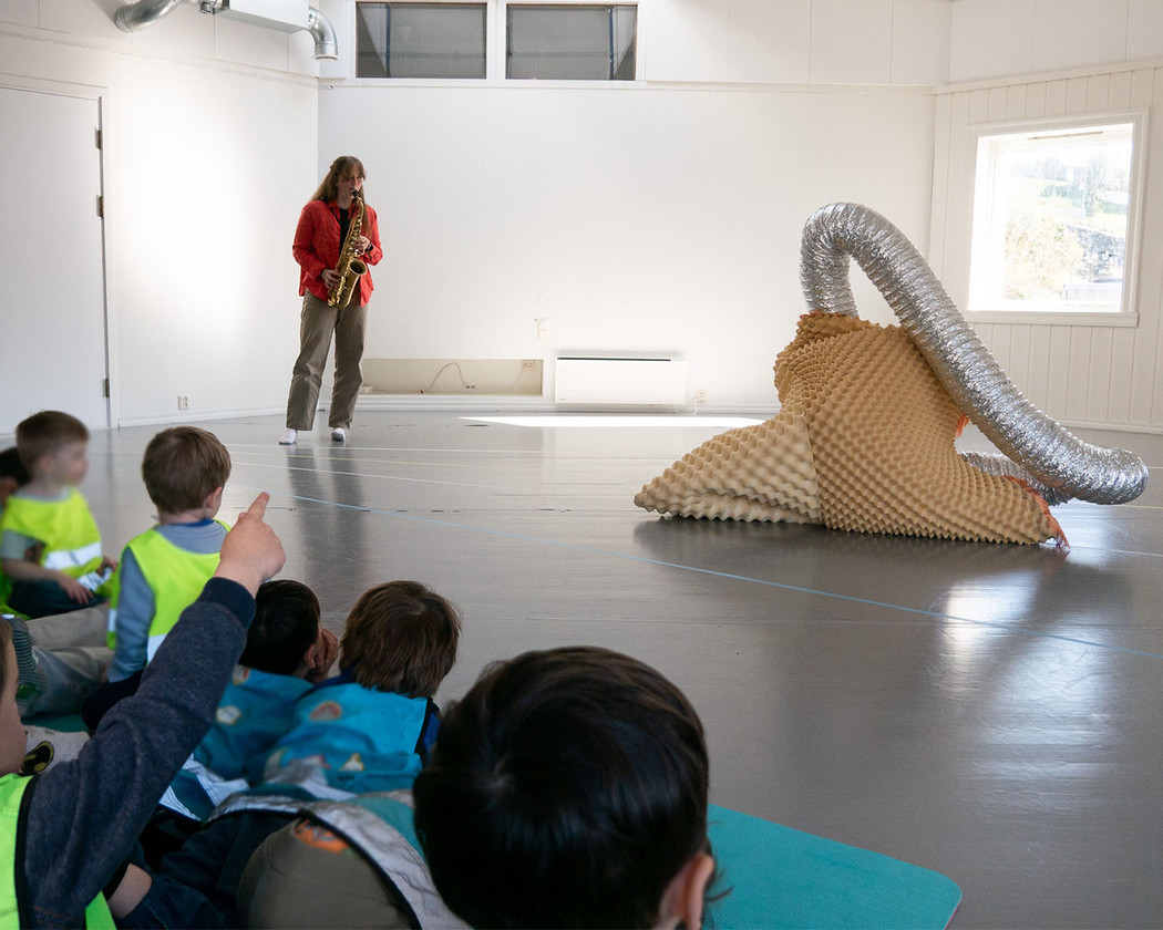 A musicican plays the saxofon while an amorph object, a fantastical creature, moves to the music. Children are the musical performance. 