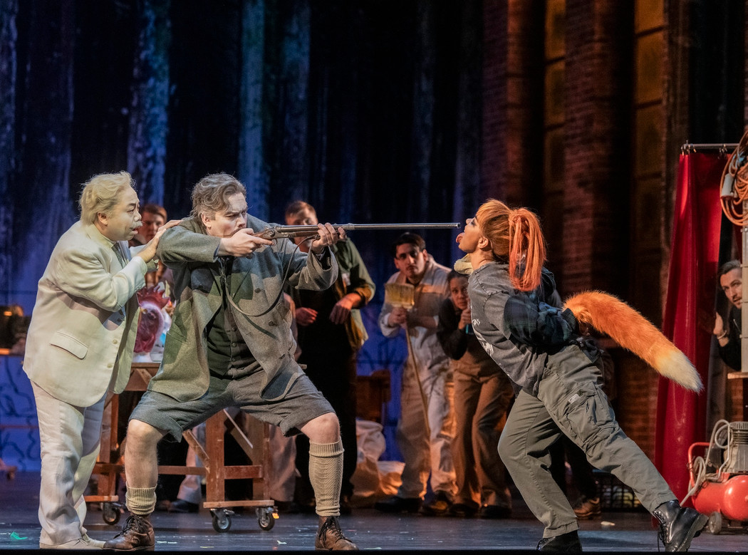 A scene from an opera where a man holds a shotgun against an actor dressed as a fox. 