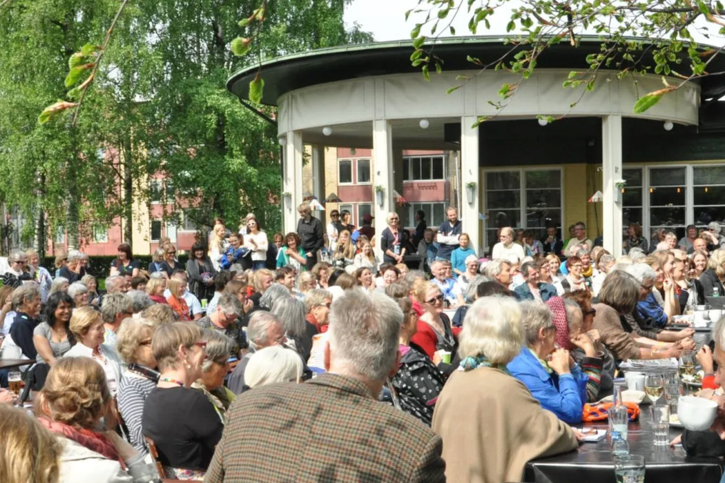 A large crowd of people in front an outdoor stage set in a green public park. 