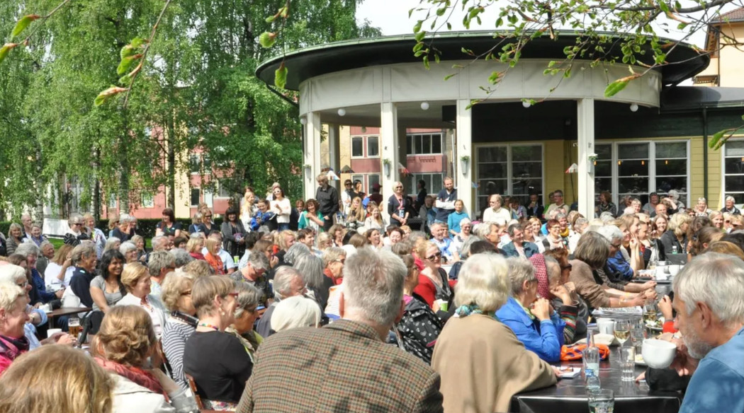 A large crowd of people in front an outdoor stage set in a green public park.