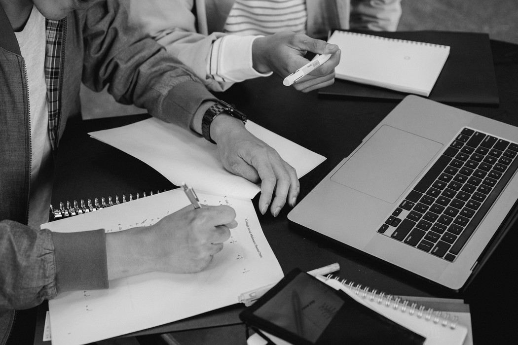 Two people around a table with notebooks, pens, and a laptop. 